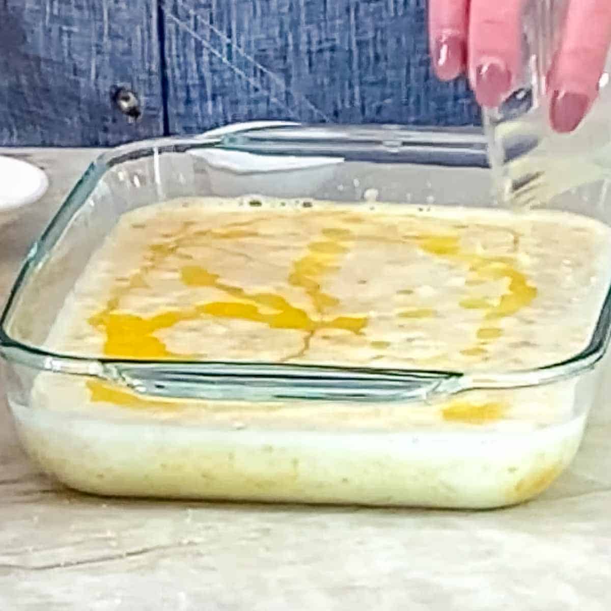 person pouring butter on top of corn mixture for corn pudding