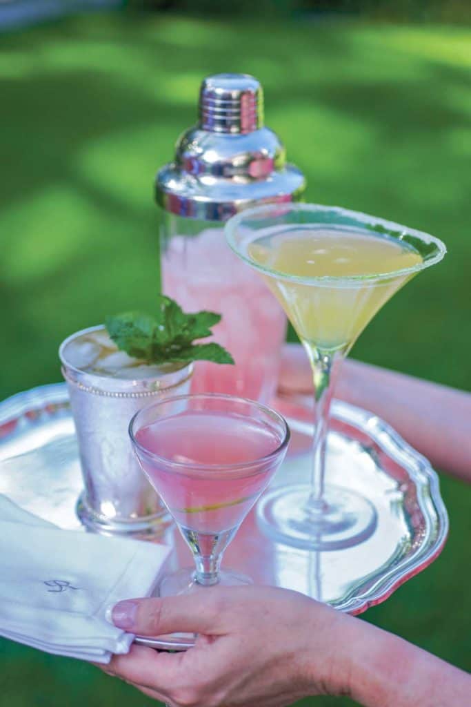 hands holding a silver tray filled with three cocktails, including a Cosmopolitan Martini in the front