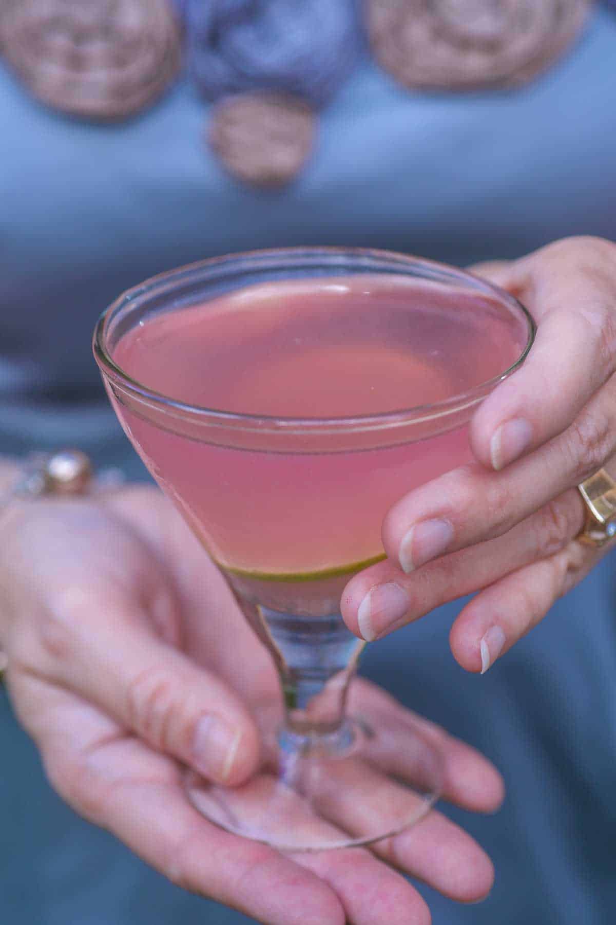 a hand holding a Cosmopolitan Martini. Person is in background.
