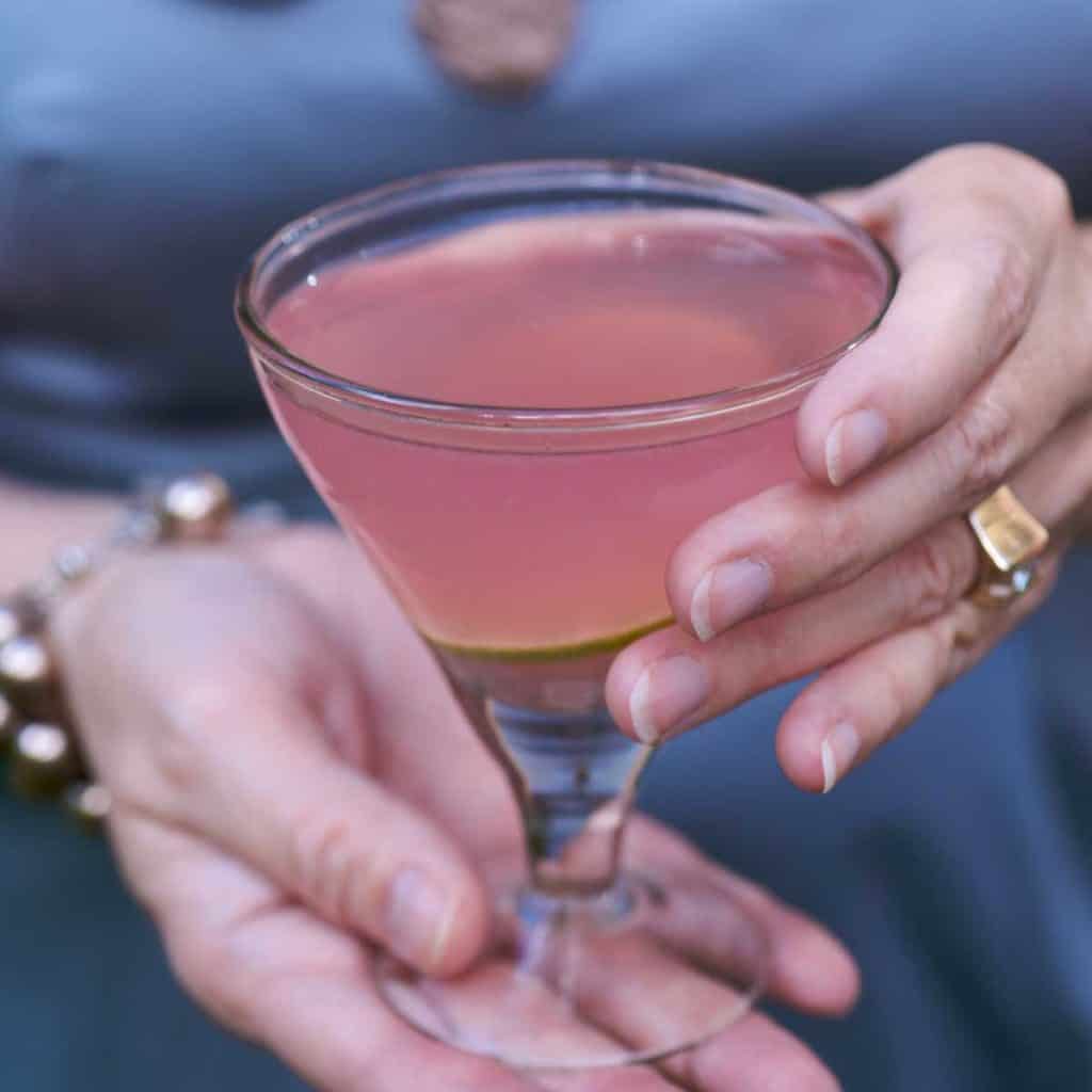 Hands holding a Cosmopolitan Martini. Person is in background