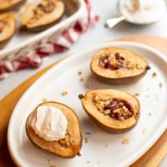 white oval plate with halved pears stuffed with cranberries and walnuts, topped with cinnamon whipped cream
