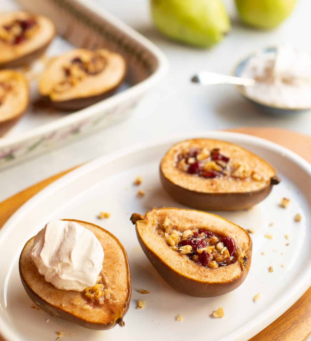 white plate with halved pears stuffed with cranberries and walnuts, topped with cinnamon whipped cream