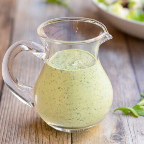 Horizontal view of a glass pitcher holding creamy salad dressing recipe showing its smooth, creaminess.