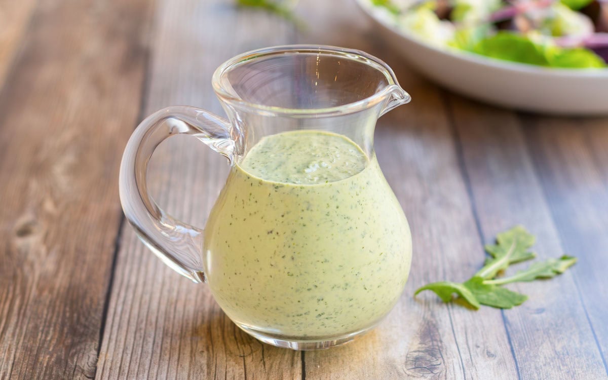Horizontal view of a glass pitcher holding creamy salad dressing recipe showing its smooth, creaminess.
