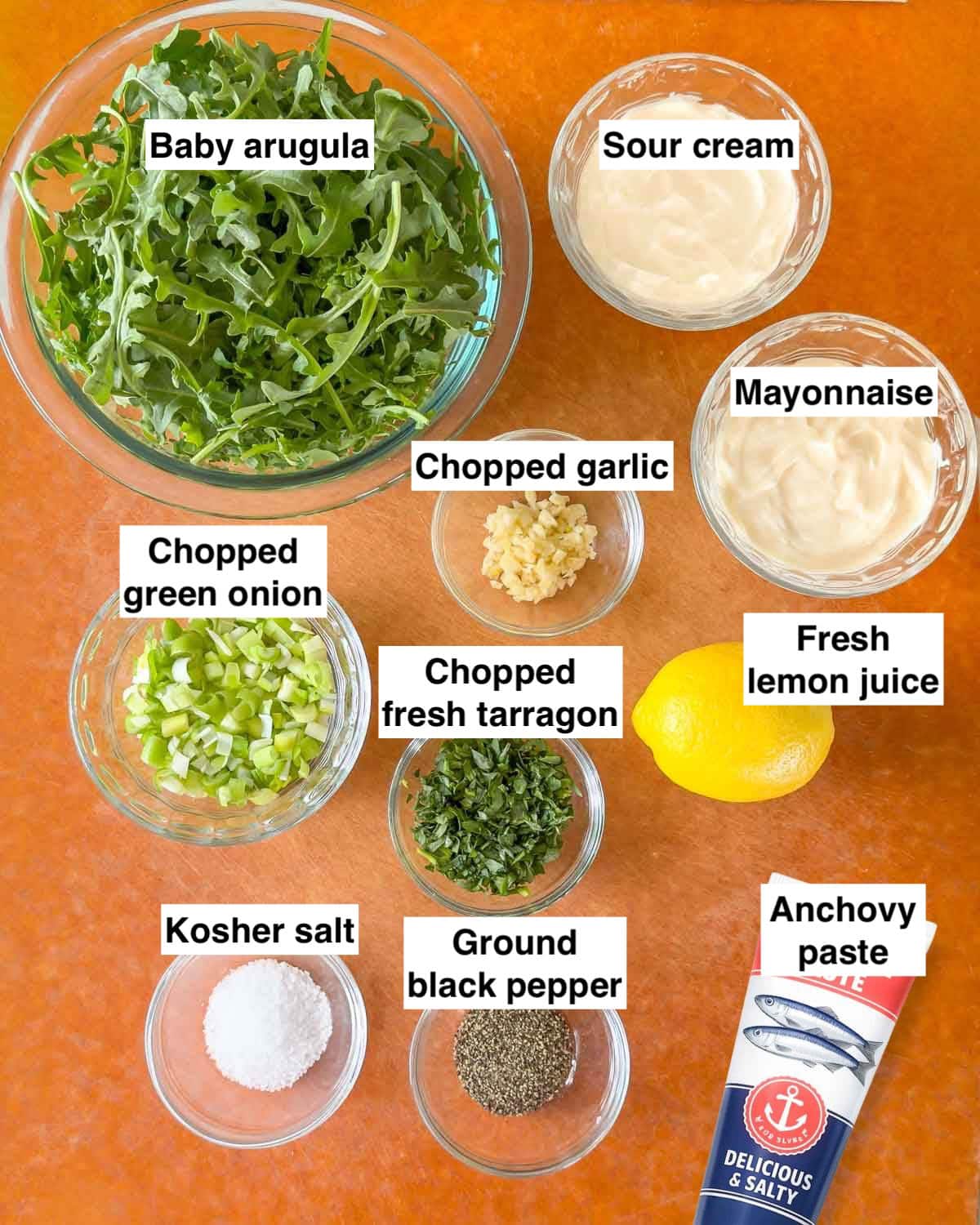 Prepared ingredients for creamy salad dressing with arugula, arranged on a cutting board, and labeled.