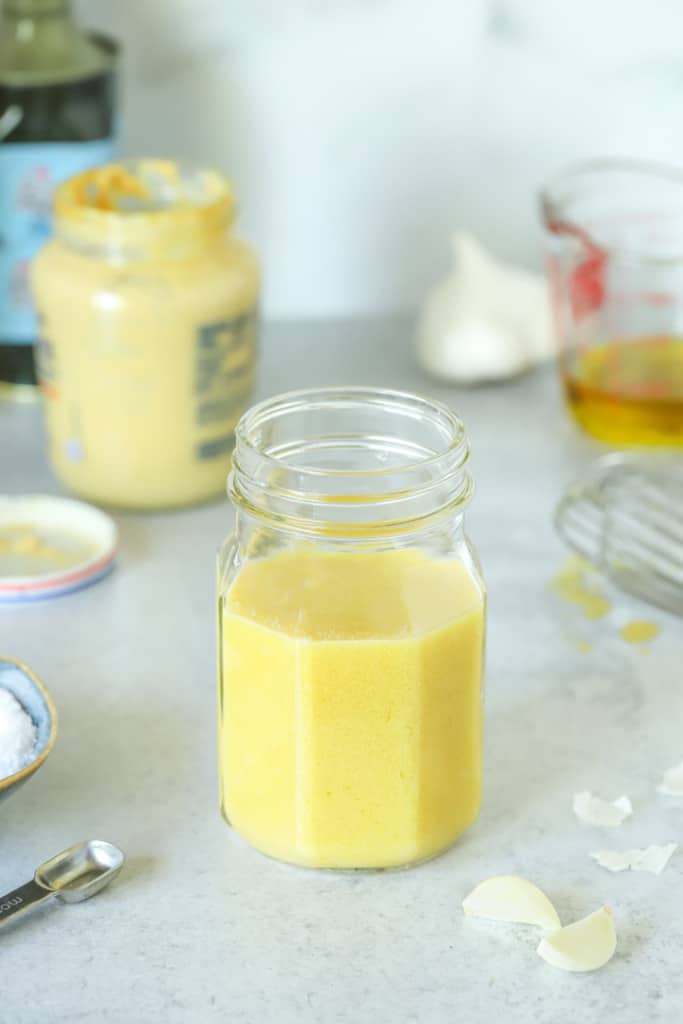 Mason jar filled with Dijon Mustard Vinaigrette, surrounded by its ingredients