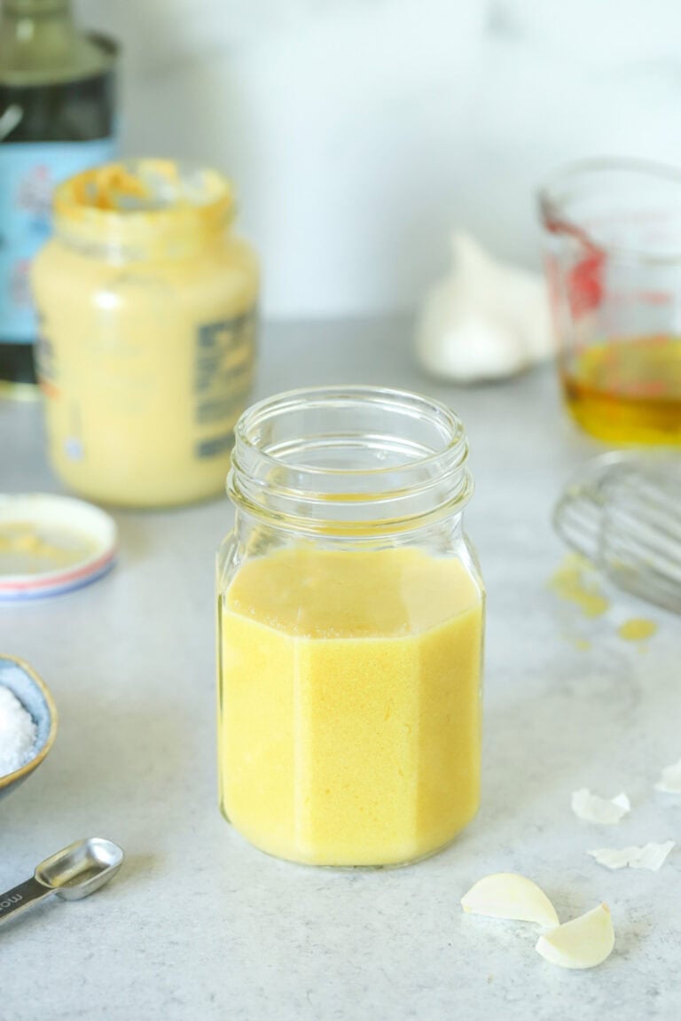 mason jar holdng mustard vinaigrette, with mustard and other ingredients in the background.