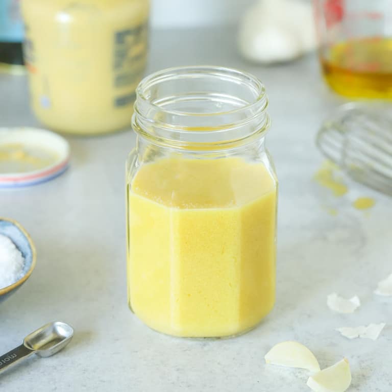 Mason jar filled with Dijon Mustard Vinaigrette, surrounded by its ingredients