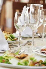 table filled with wine glasses, plates of salad and white napkins