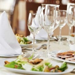 table filled with wine glasses, plates of salad and white napkins