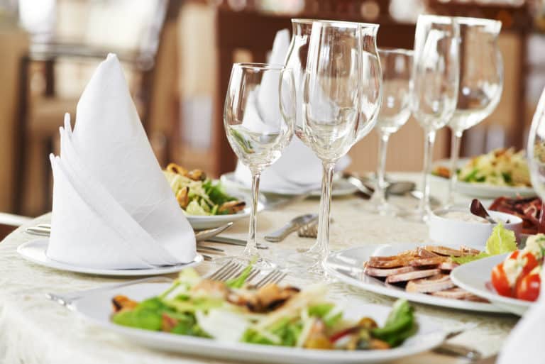 table filled with wine glasses, plates of salad and white napkins