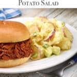 White plate with Dorothy's Potato Salad sitting next to a BBQ Beef Sandwich