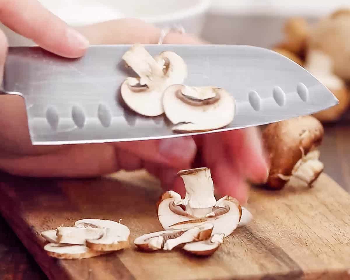 close up of knife and hand chopping mushrooms