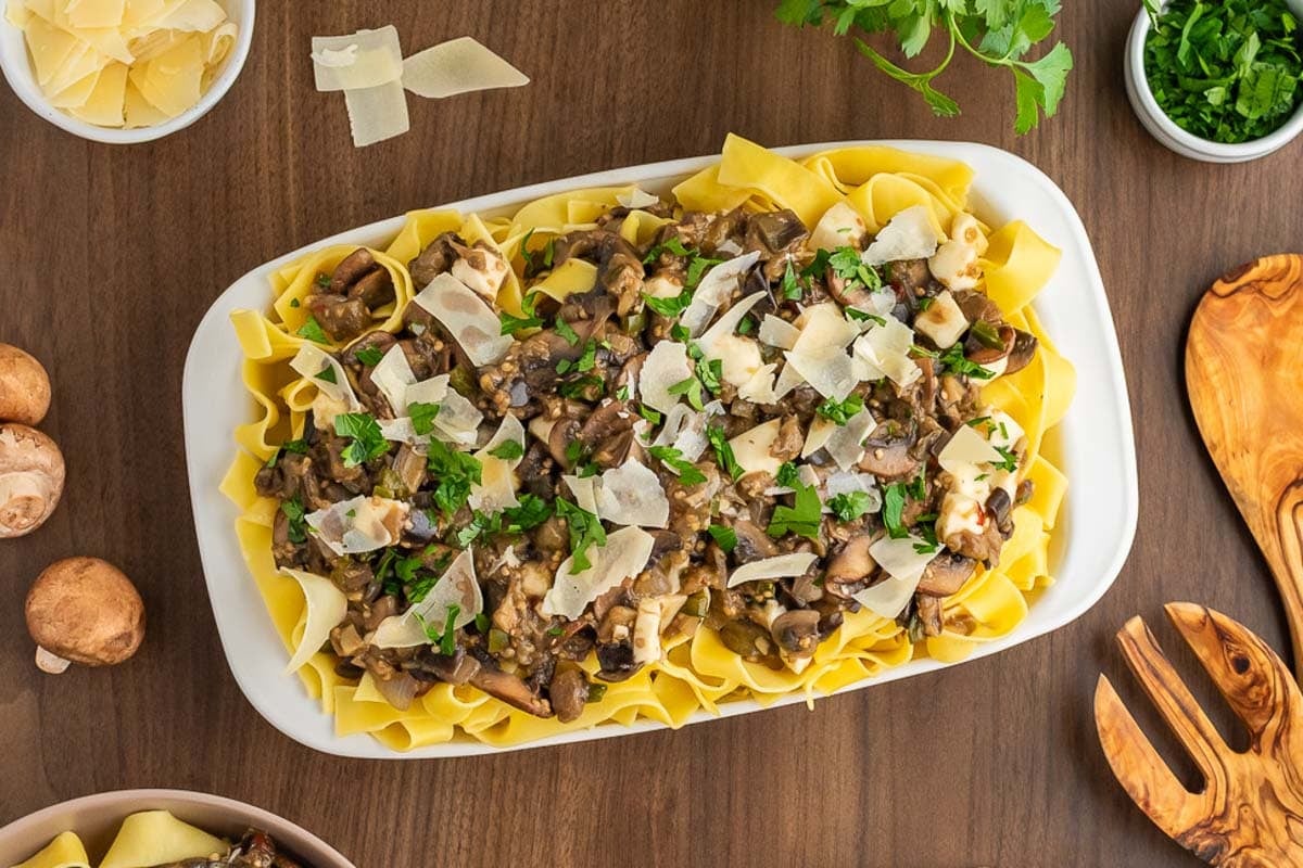 A plate of eggplant and mushroom pasta garnished with parsley and shaved Parmesan.