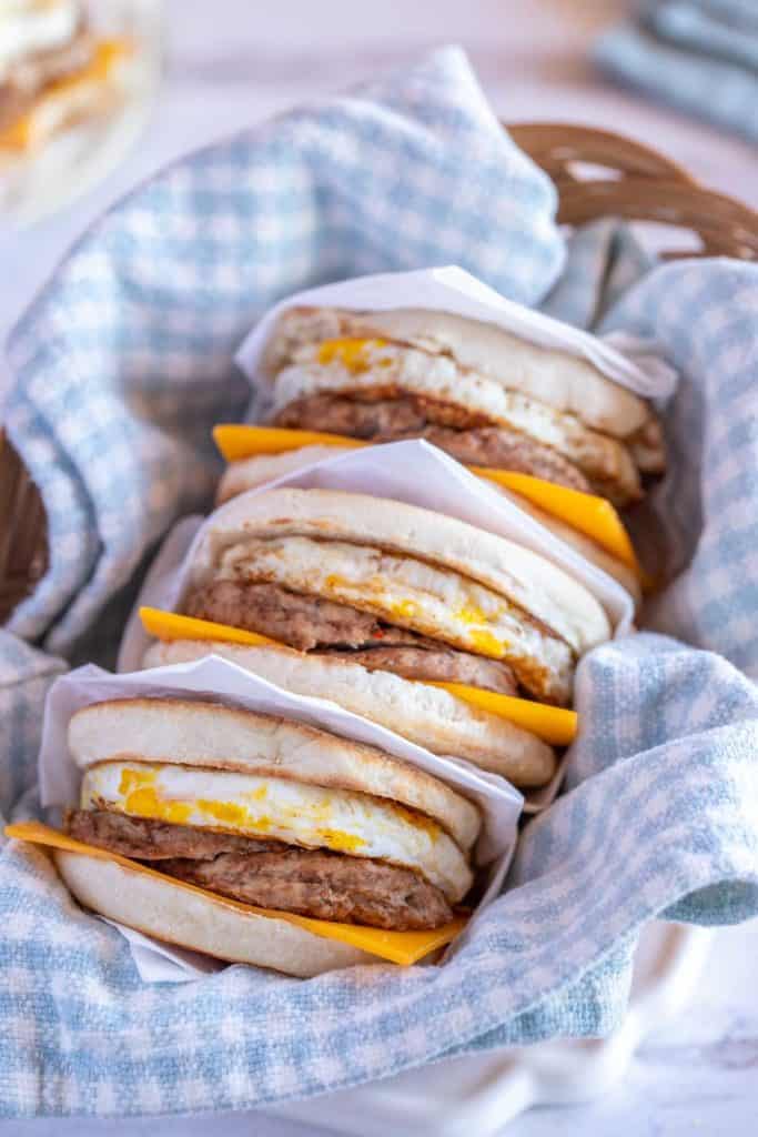 Basket filled with a blue and white dish towel holding three freezer Breakfast Sandwiches with Egg