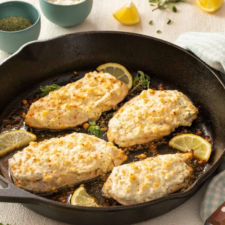 Cast iron skillet holding 4 Feta Chicken Breasts, with various ingredients surrounding the pan