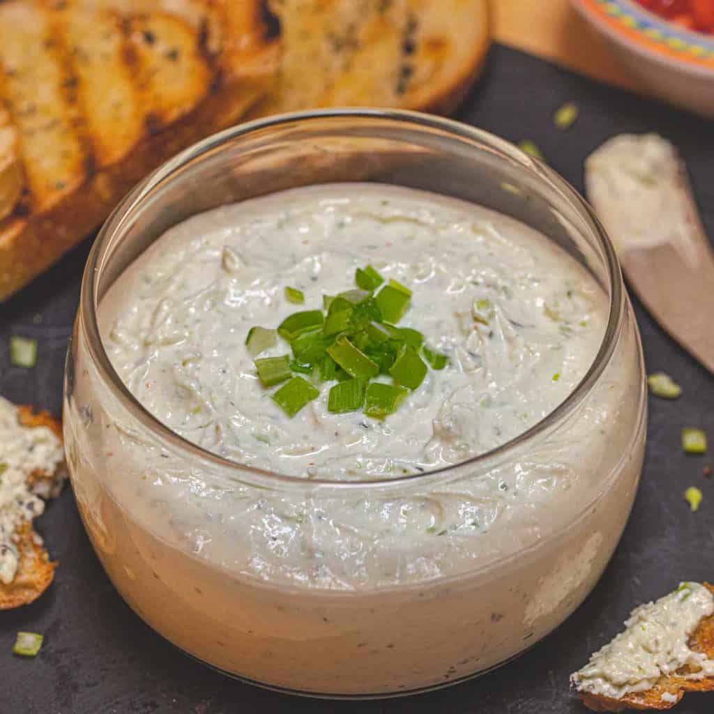Glass bowl filled with Feta Mousse on black tray with grilled bread
