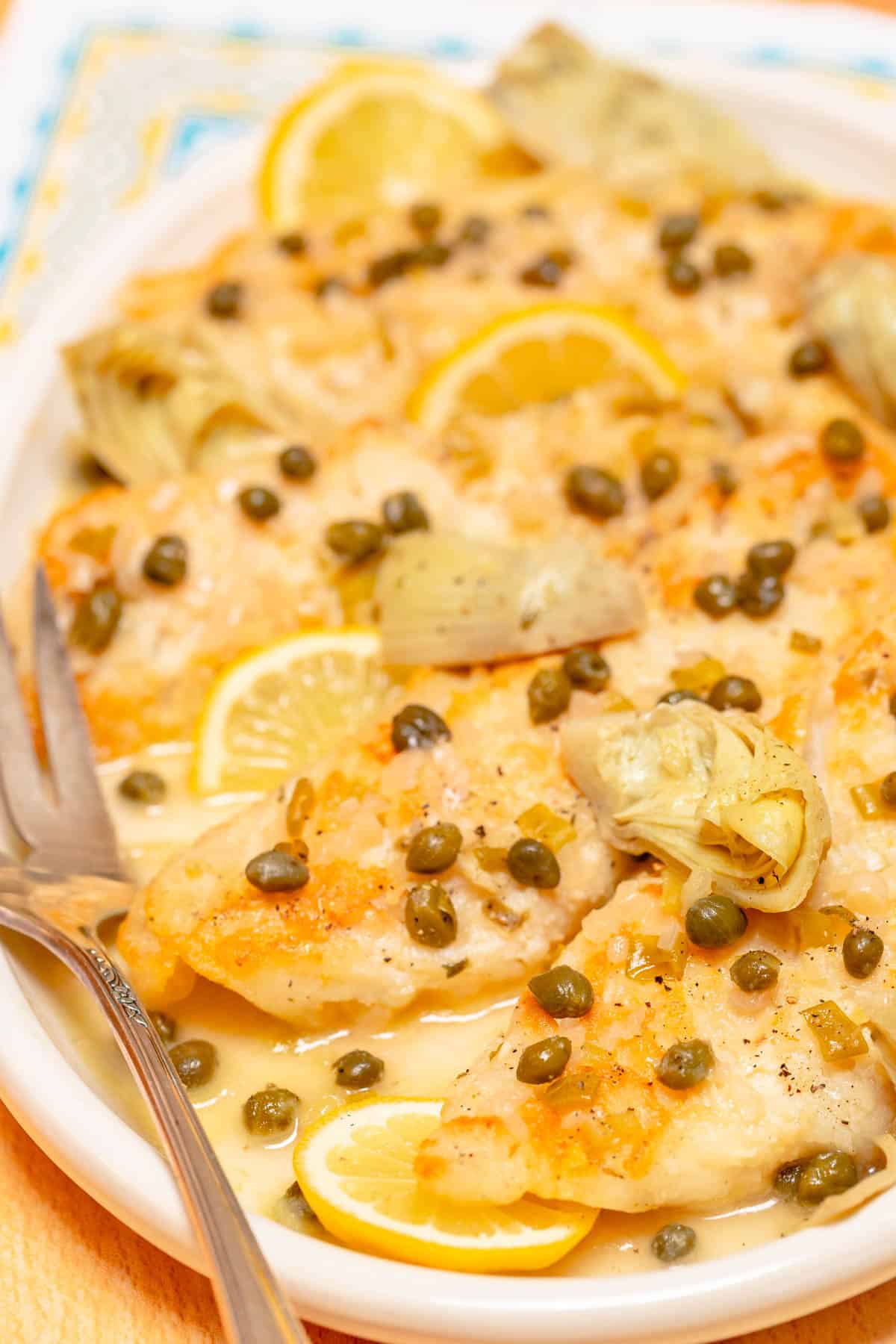 large white platter holding several portions of White Fish Piccata with Artichokes