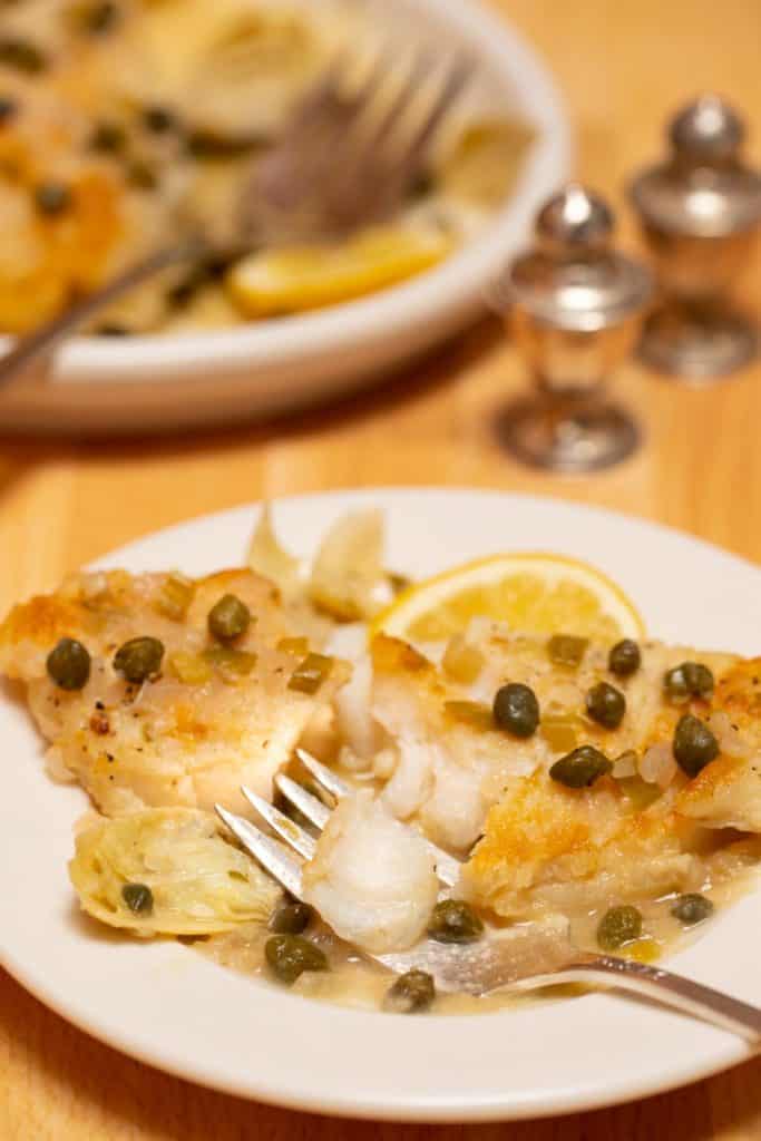 piece of Easy Fish Piccata with Artichokes on a white plate with a fork