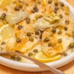Close up of fish piccata with capers and artichokes.