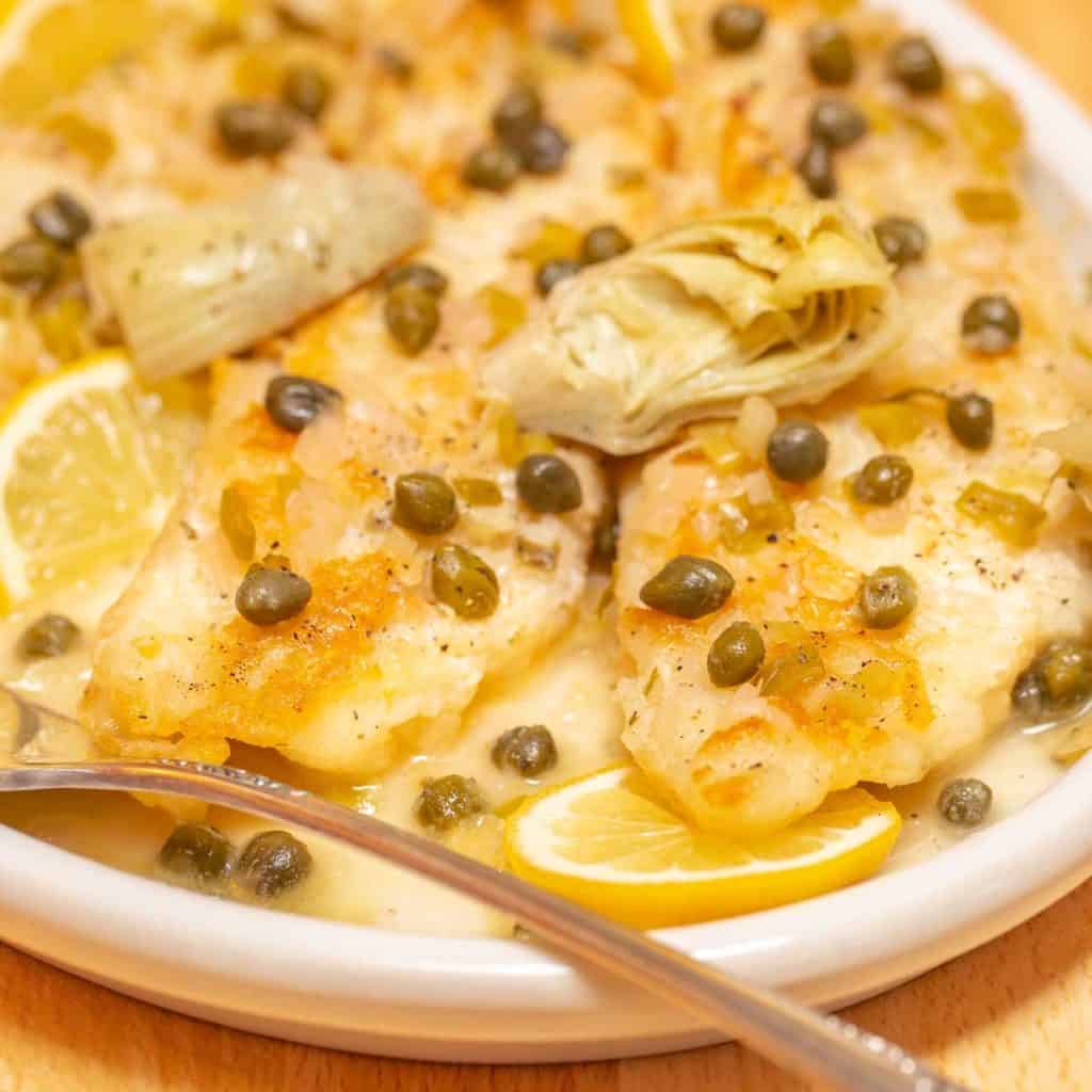 close up of a white platter holding portions of White Fish Piccata