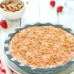 Deep dish blue pie plate showing a Frozen Strawberry Pie with walnuts in a bowl in the background