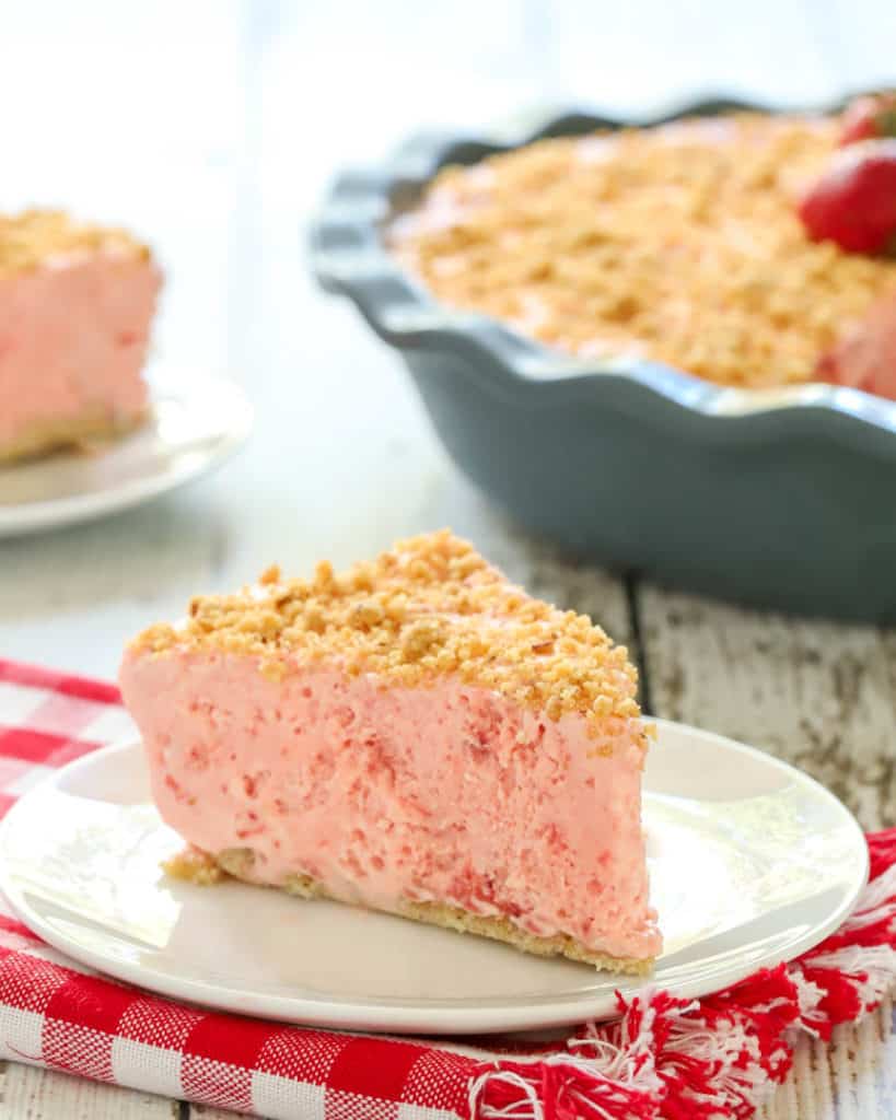 slice of Frozen Strawberry Pie on a plate with the rest of the pie in the background