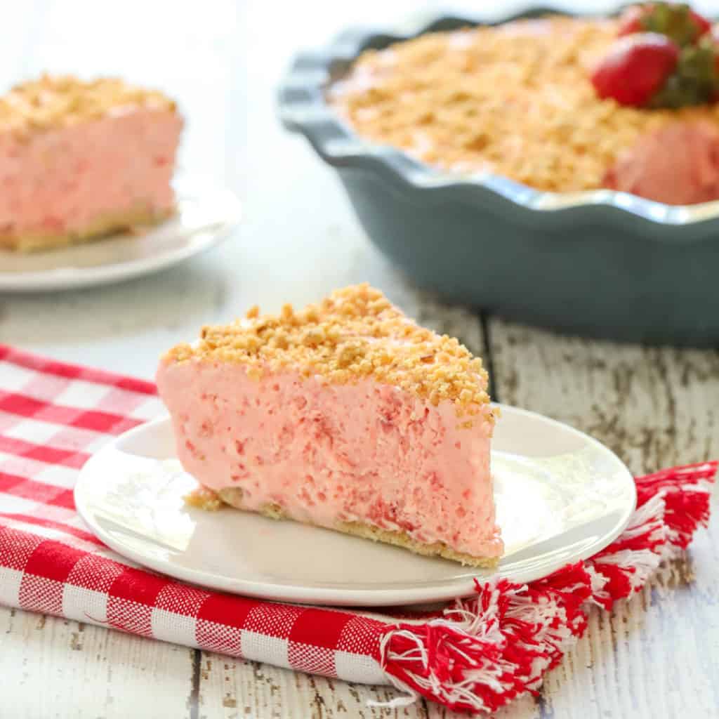 slice of Frozen Strawberry Pie on a white plate with rest of pie in the background