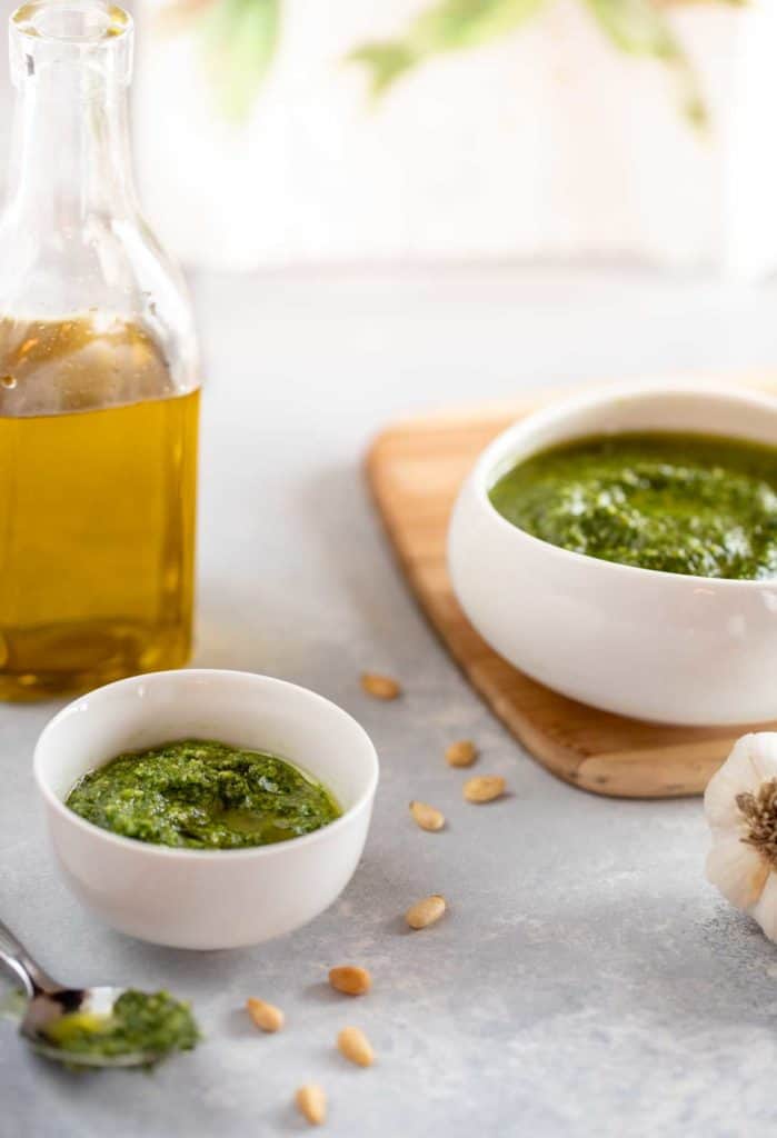 Two white bowls, one small and one larger, holding Pesto Genovese, with a bottle of olive oil