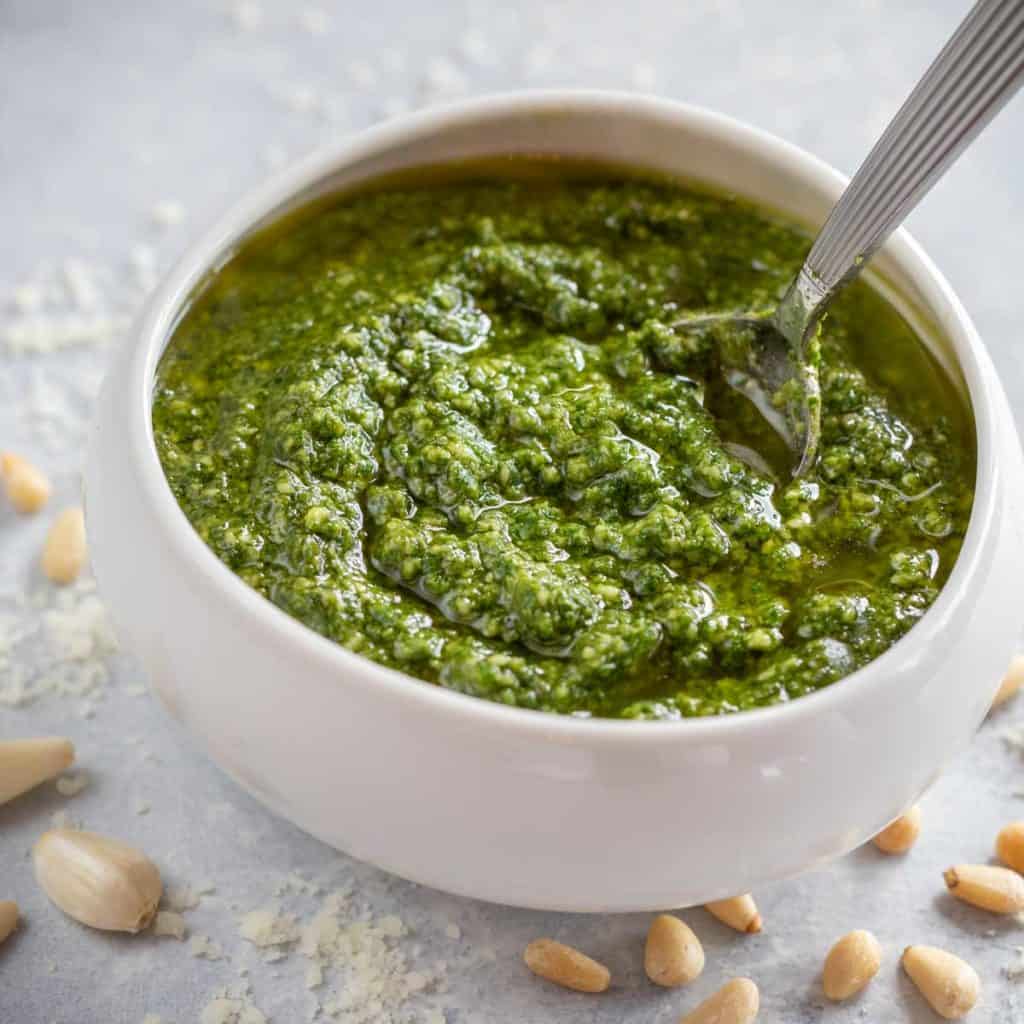 close up of a white bowl holding Pesto Genovese, with a spoon in the pesto