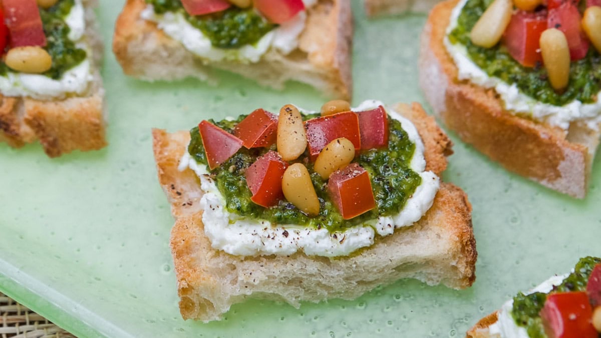 close up of a few pieces of goat cheese, pesto, tomato crostini