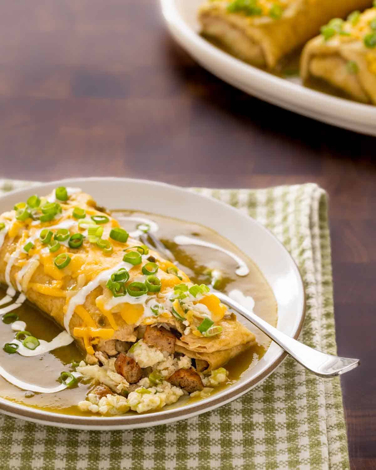 plate holding one breakfast burrito smothered in green chile sauce, with a corner open