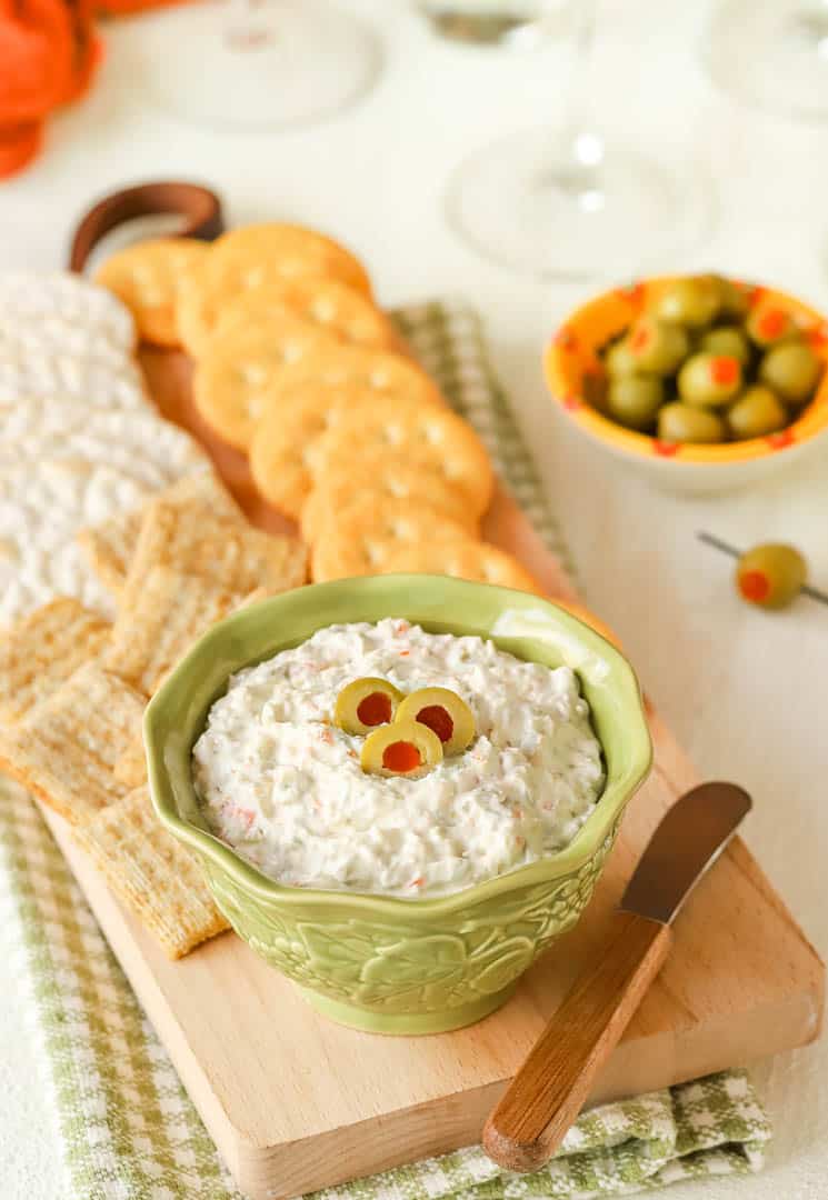 Small bowl holding Green Olive Cheese Spread, with some on a cracker in front and more crackers in back