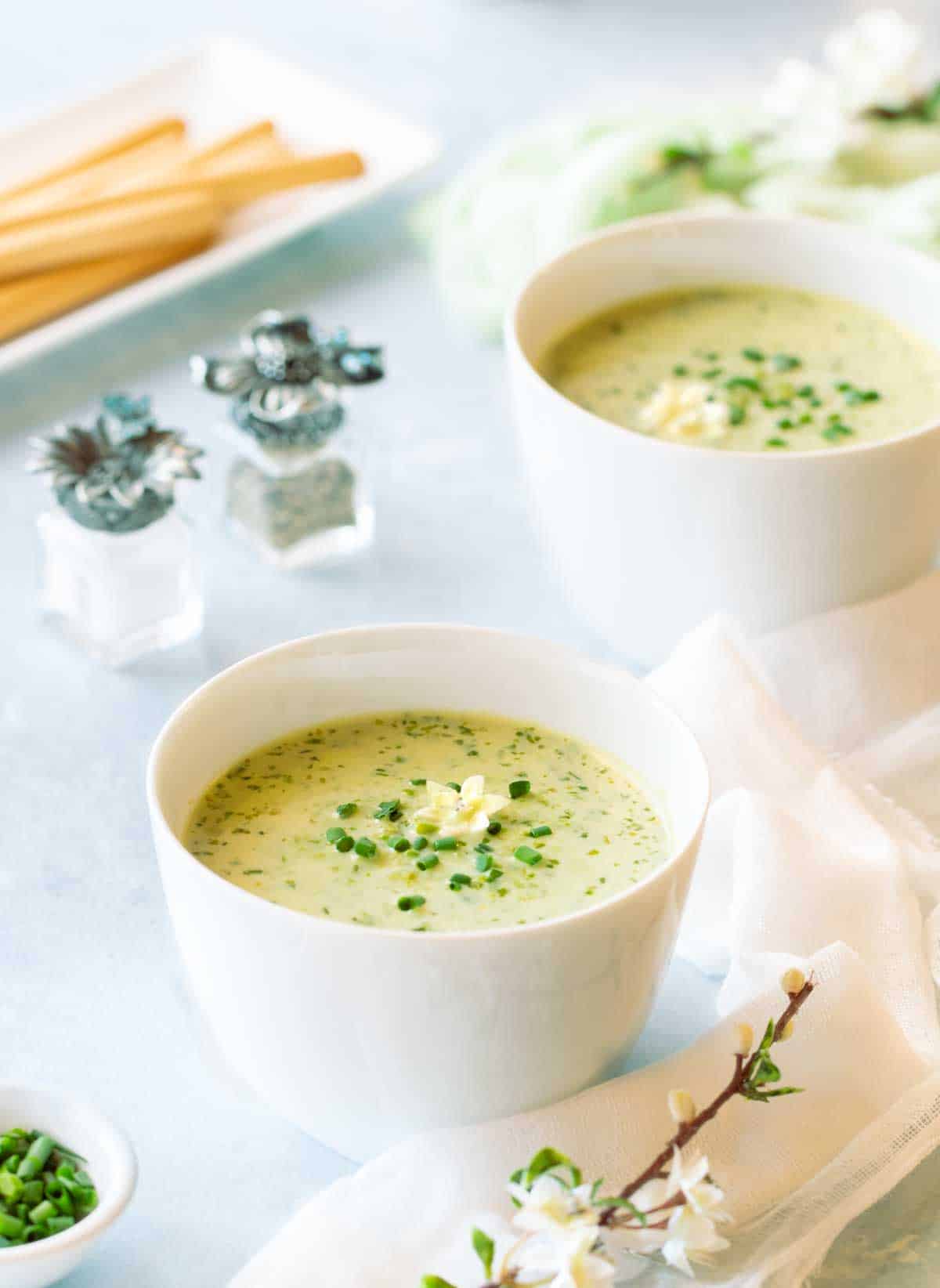 Two white bowls each holding a portion of Puréed Grean Pea Soup, with small salt and pepper shakers on the side