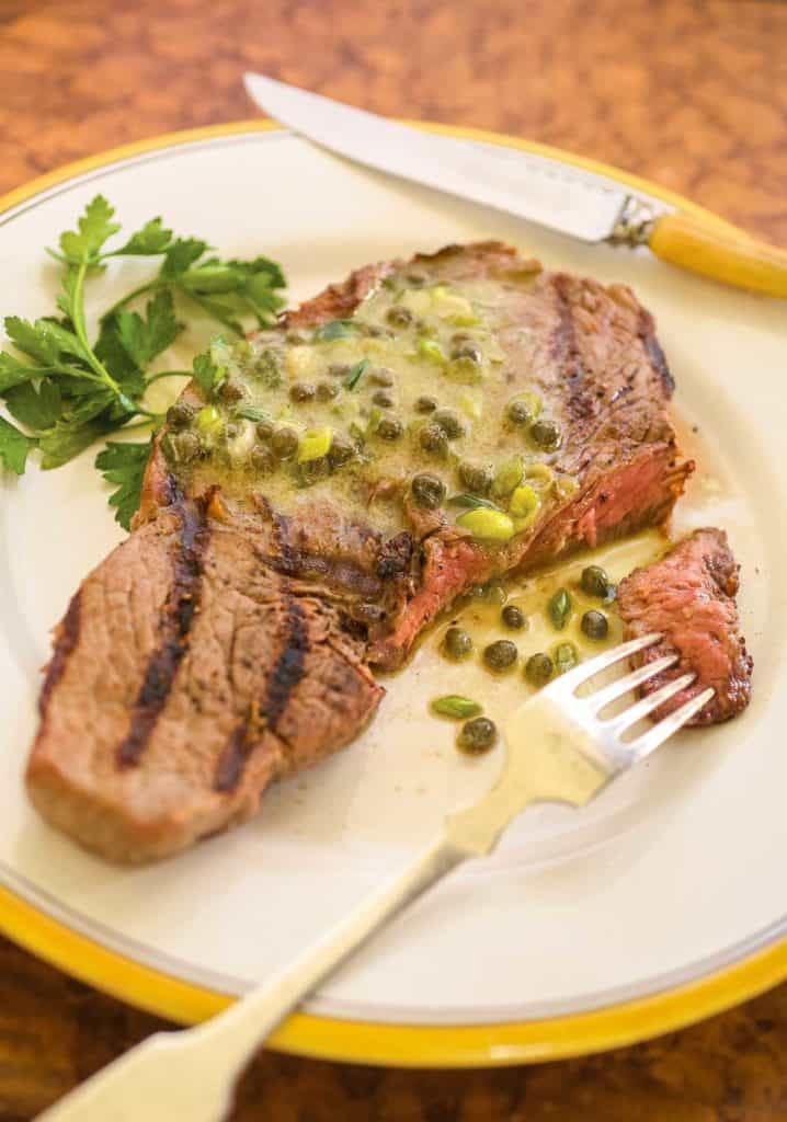 white plate showing a single Grilled Ribeye Steak, with a bite on a fork