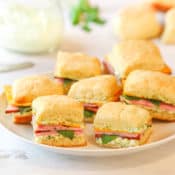 image of white plate holding several Ham and Chese Biscuits with Herb Mayo in the background