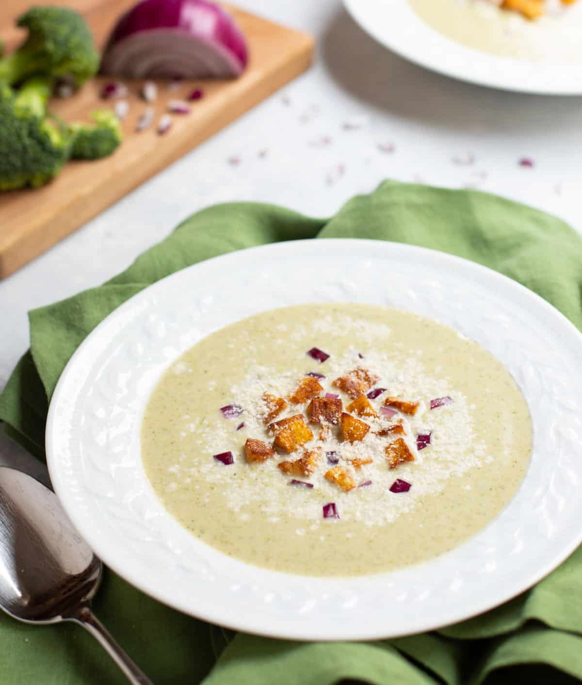 Bowl of Healthy Broccoli Soup garnished with Potato Croutons, red onion and Parmesan