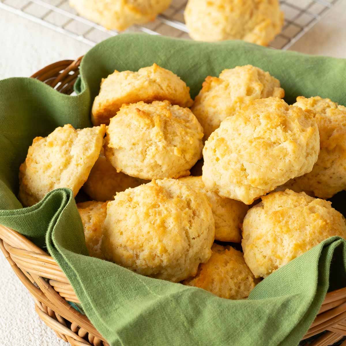 Wicker basket lined with a green napkin and filled with Easy Drop Biscuits, with a few partial biscuits in the background