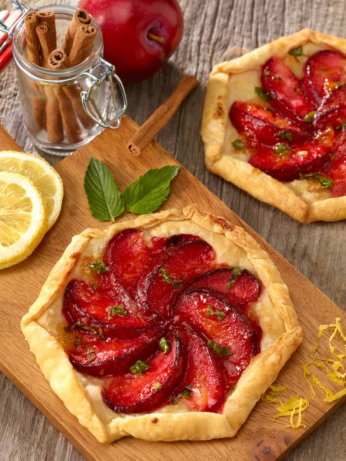 Wooden board holding an Individual Plum Tart, with a second tart to the side