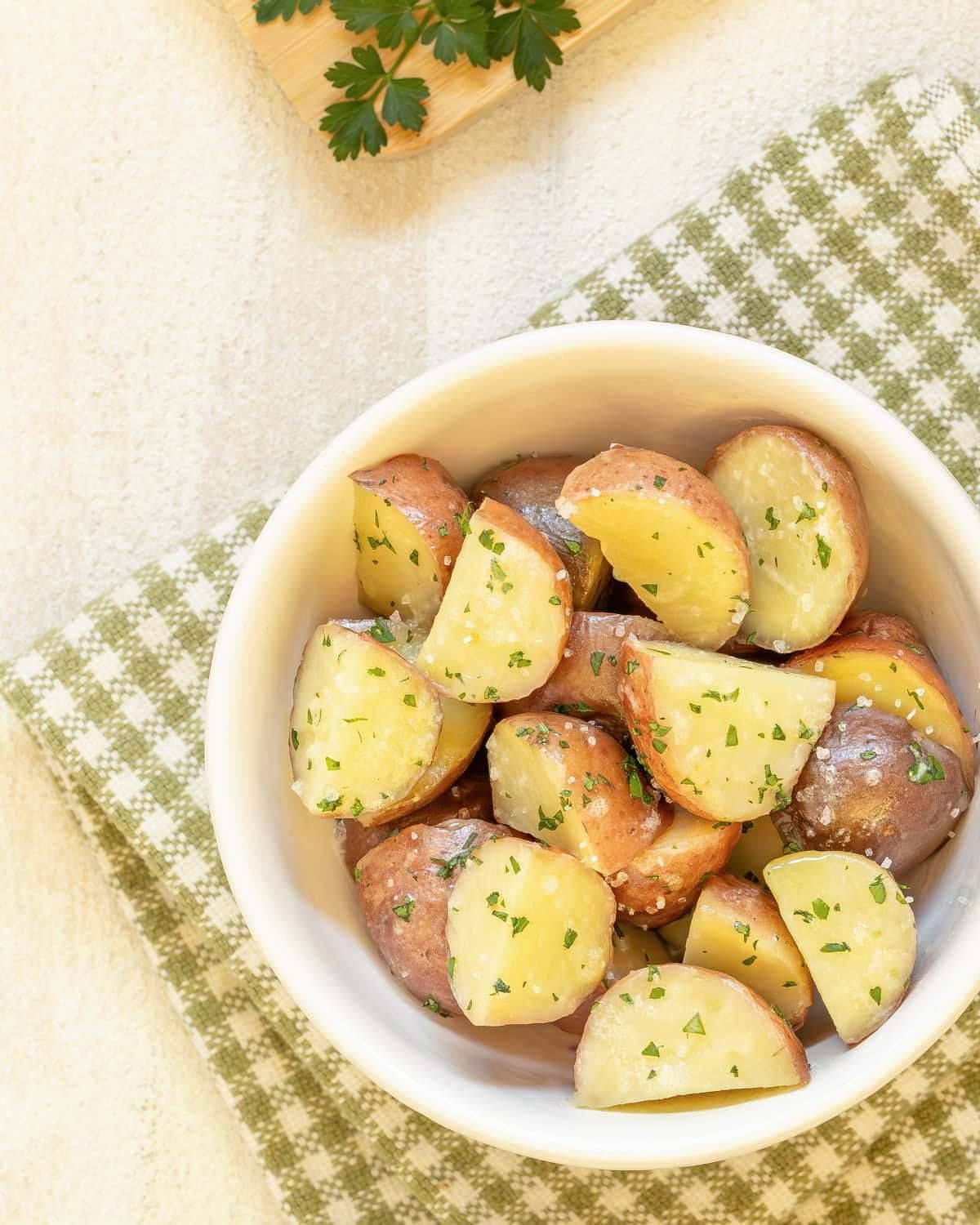 Closer view of steamed halved new potatoes that have been tossed with melted butter, parsley, and kosher salt.