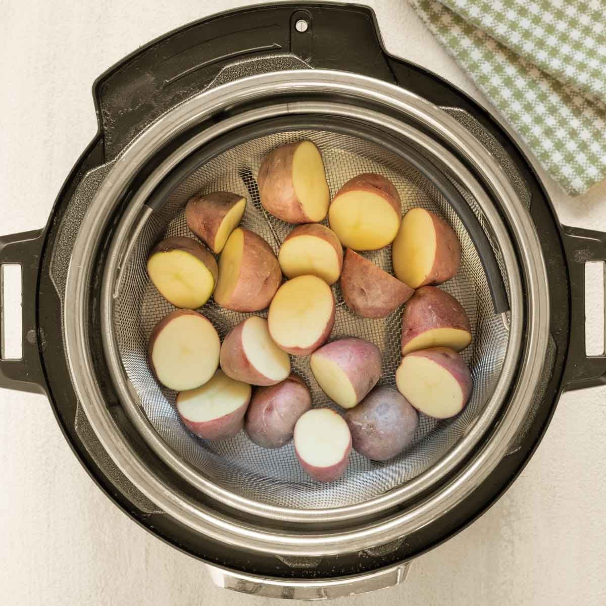 Halved small red potatoes inside Instant Pot, in steamer basket over water, ready to steam.
