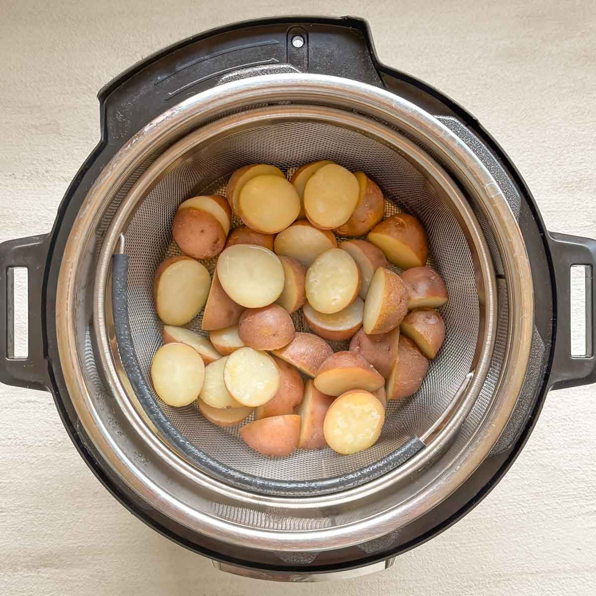 Steamed halved small red potatoes inside Instant Pot, in steamer basket.