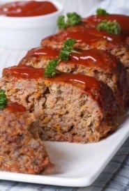 Italian meatloaf on a platter, with a few slices in front to show inside.