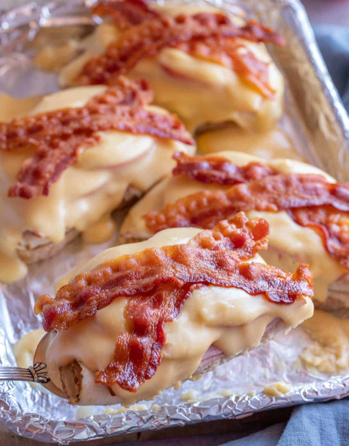 Baking sheet holding 2 cooked Kentucky Hot Brown sandwiches with a spatula holding up another one for a closer view.