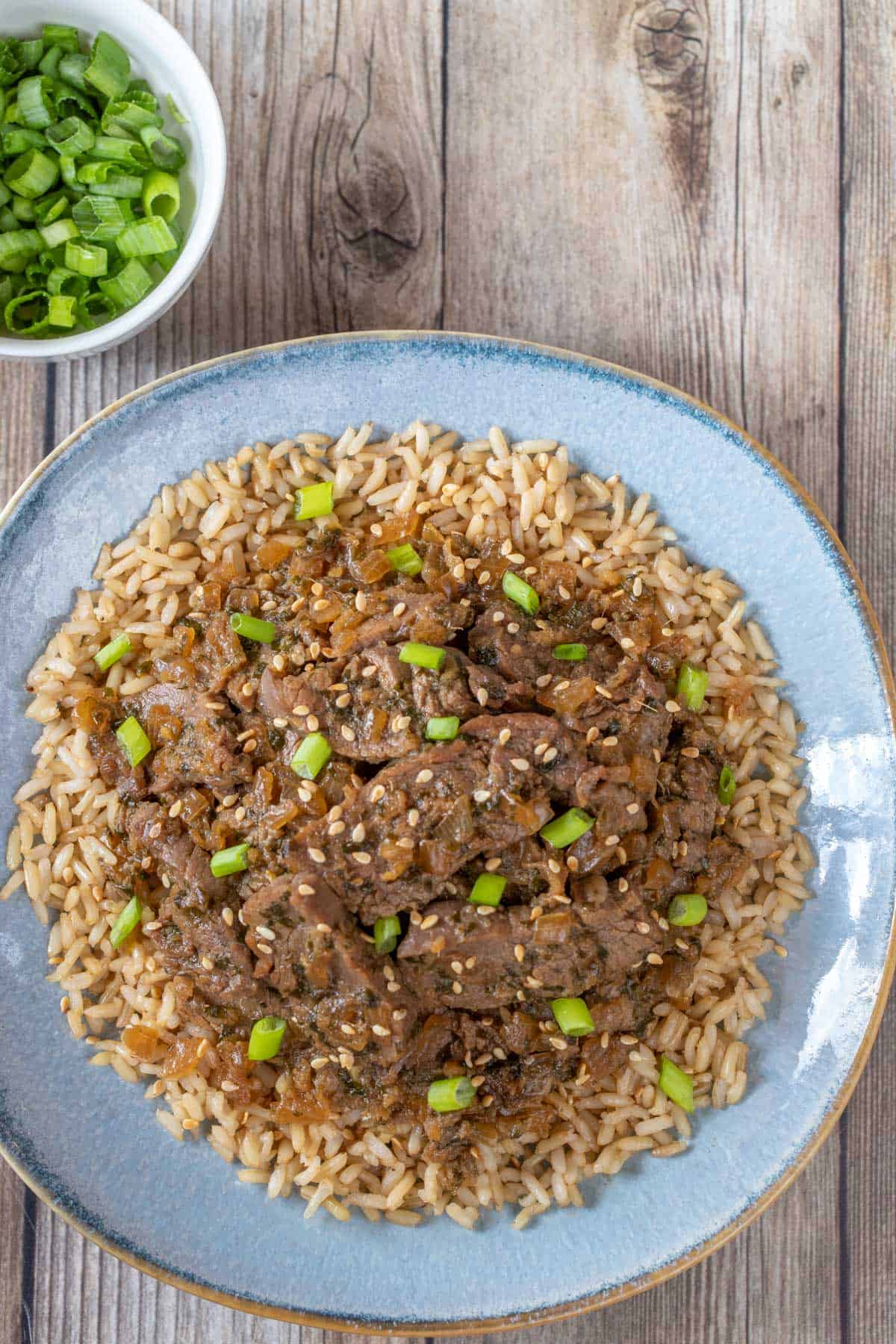 blue plate holding Korean BBQ Beef over brown rice. Plate is on a wood background