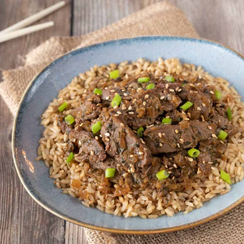 Blue plate showing Korean BBQ Beef over brown rice. Place is sitting on a napkin