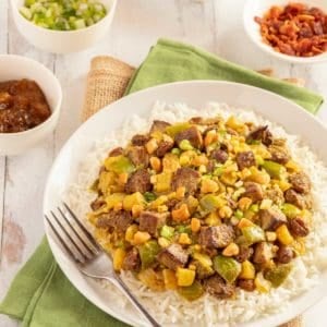 white plate holding Lamb Curry, with 4 small bowls alongside, showing condiments