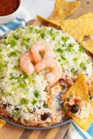 Layered Shrimp Cocktail Dip with tortilla chips on a blue plate