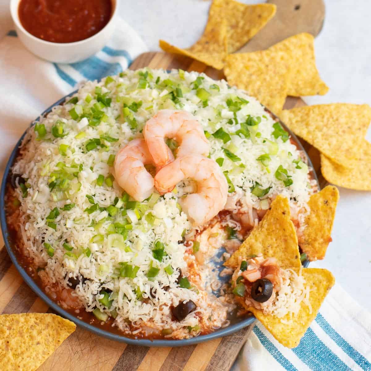 Layered Shrimp Cocktail Dip with tortilla chips on a blue plate