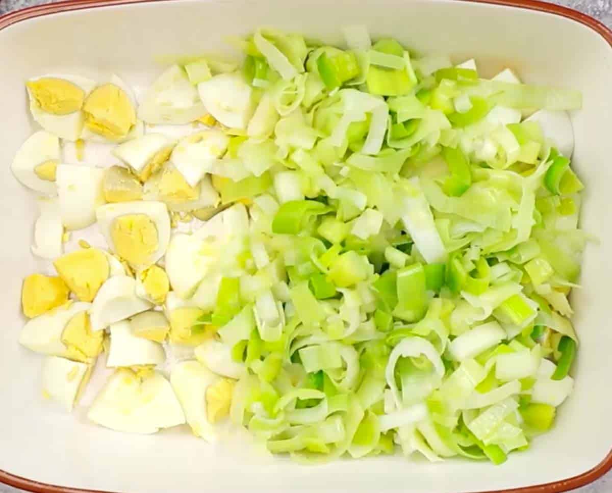 baking dish with cooked leeks being placed on top of hard-boiled eggs